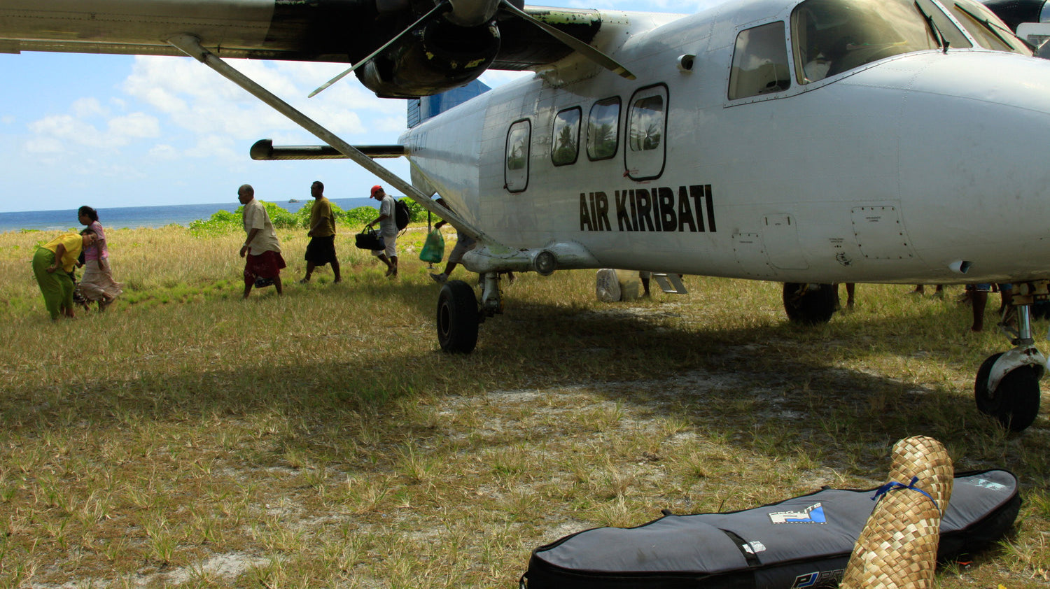 Pro-Lite finless coffin surfboard travel bag on ground next to small airplane.