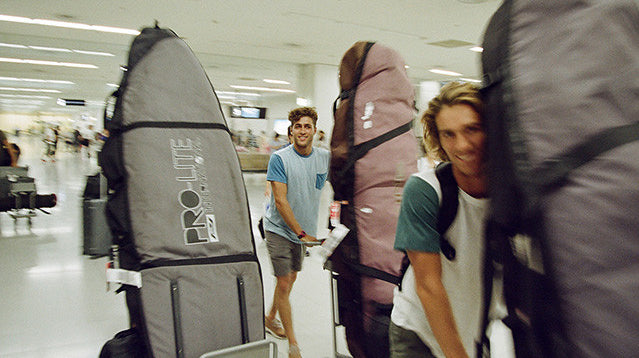 A group of surfers push their surfboard travel bags through an airport.