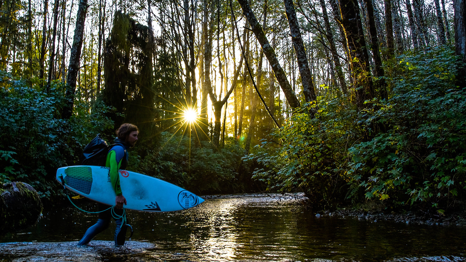 Timmy Reyes crosses creek with surfboard.