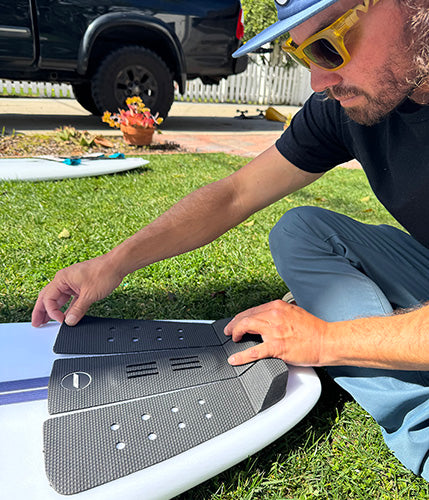 Timmy Reyes applying surfboard traction pad on a surfboard outdoors.