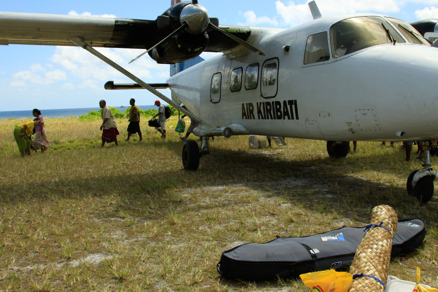 Pro-Lite finless coffin surfboard travel bag on ground next to small airplane.