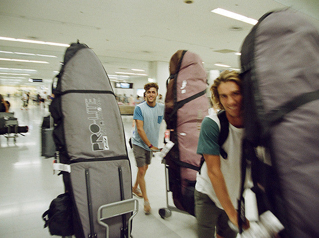 A group of surfers push their surfboard travel bags through an airport.