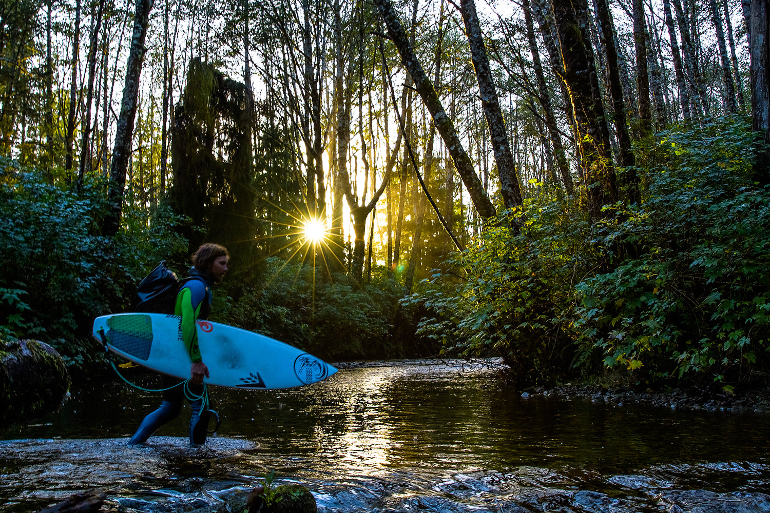 Timmy Reyes crosses creek with surfboard.