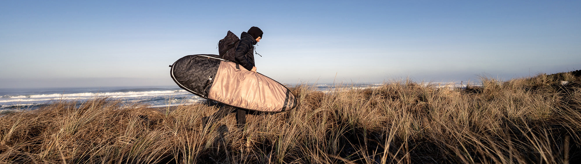 Person walking with surfboard day bag fish/hybrid at beach.