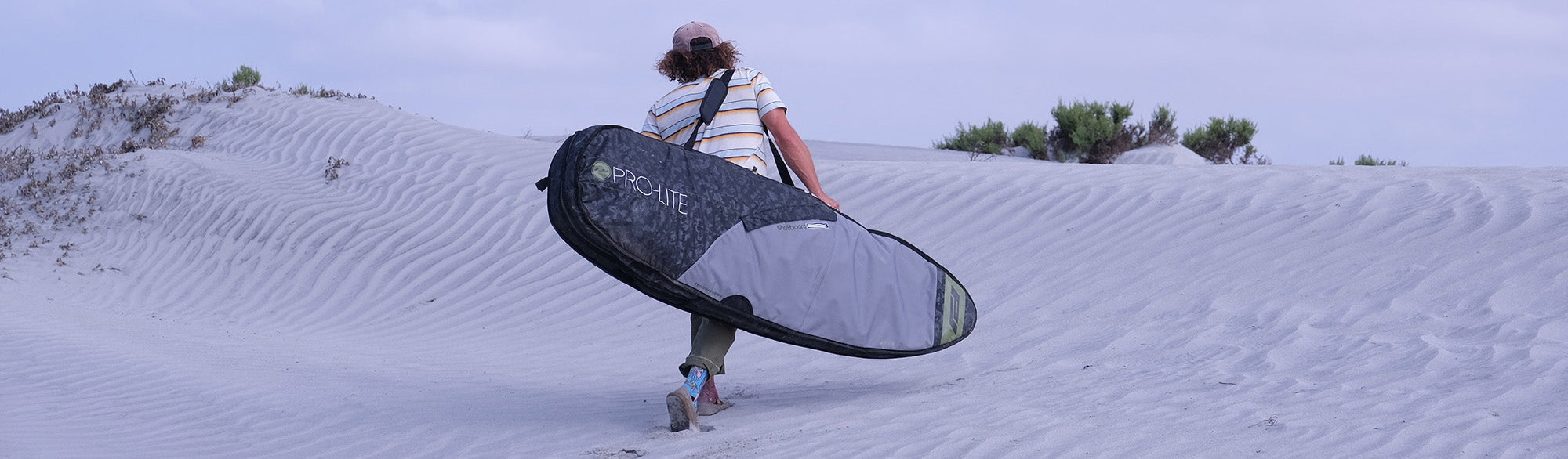 Timmy Reyes walks over sand dune with rhino double surfboard travel bag.