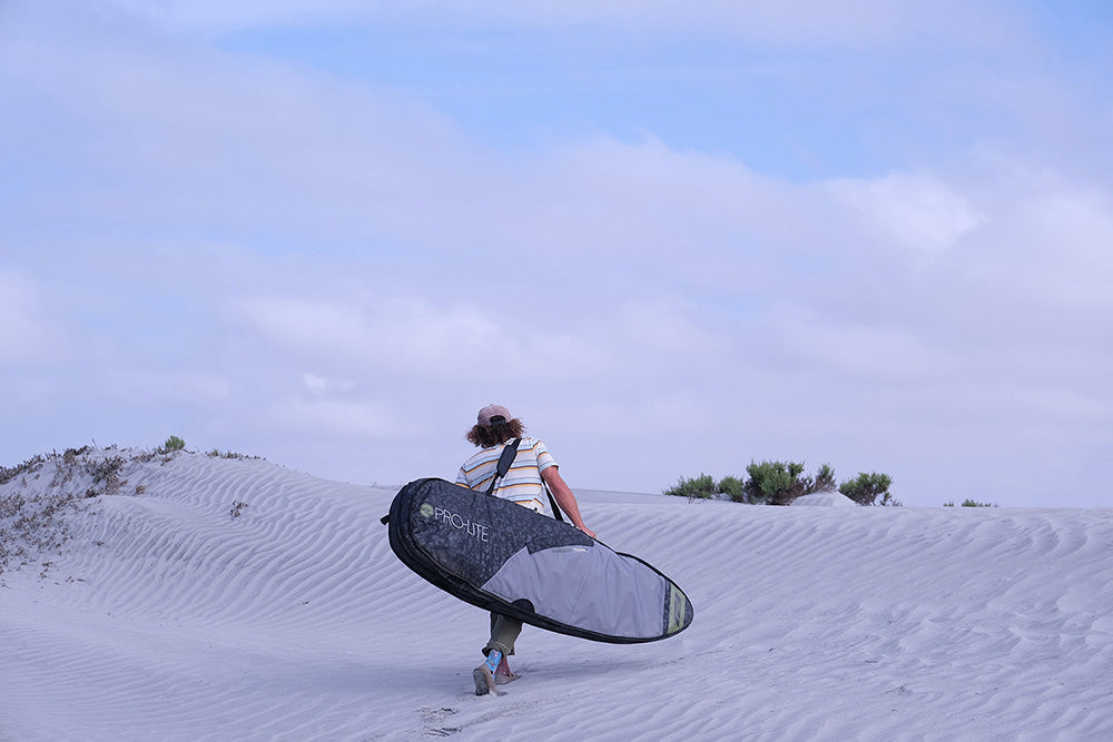 Timmy Reyes walks over sand dune with rhino surf travel bag.