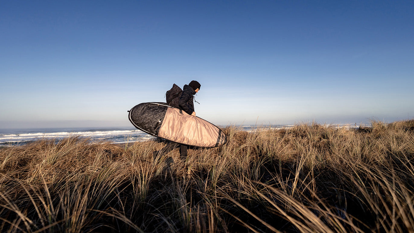 Surfer walking on beach with session fish hybrid bag.